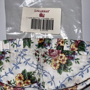 May include: A white fabric liner with a floral pattern in shades of blue, yellow, green, and pink. The liner is for a Longaberger basket and has the text "Liner-Button Mothers Day (IT) 2143755" on a label.