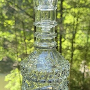 May include: A clear glass bottle with a textured design. The bottle has a wide base and a narrow neck with a decorative top.
