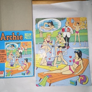 May include: A 100-piece jigsaw puzzle featuring the Archie comic characters. The puzzle depicts the characters at a pool party, with a pool, lounge chairs, and a radio. The puzzle box is red, white, and blue with the Archie logo and the text "100 interlocking pieces 14 x 18 inch puzzle".