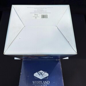 May include: A white cardboard box with a folded top, featuring text from Westland Giftware and Disney. The box is on top of a dark blue box with the Westland Giftware logo. The box has a warning label.