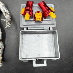 May include: A silver and gold action figure with red and yellow Iron Man armor pieces. The armor pieces include gauntlets, a helmet, and a gray plastic case.