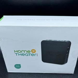 Könnte beinhalten: Weiße Box mit grünen Akzenten und der Aufschrift "4K Ultra HD Home Theater Box". Die Box zeigt die Worte "Home Theater Box" in Grün und ein schwarzes Gerät mit demselben Text.