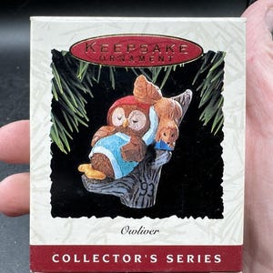 May include: A boxed "Keepsake Ornament" from the Collector's Series. The ornament features an owl wearing a blue shirt and a brown hat, perched on a tree branch with a smaller animal. The box has text that reads "Owlver" and "93".