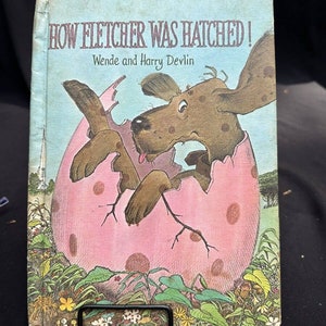 May include: A vintage children's book titled "How Fletcher Was Hatched!" by Wende and Harry Devlin. The cover features a brown and white dog emerging from a pink egg with polka dots.