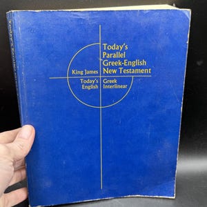May include: A blue hardback book titled Today's Parallel Greek-English New Testament. The cover features yellow text and a thin yellow cross design centred on the front. The spine also displays the title in yellow text against the blue background.