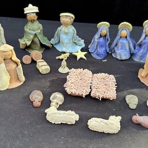 May include: A nativity scene set with ceramic figurines of Mary, Joseph, baby Jesus, three wise men, three angels, and two sheep. The figurines are painted in various shades of blue, green, yellow, and brown. The set also includes a manger, hay, and a star.