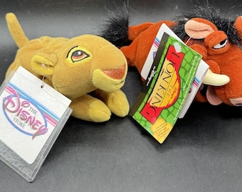 May include: Two plush toys from The Lion King. One is a yellow lion cub with a Disney Store tag. The other is a brown warthog with tusks and a Lion King tag. Both toys have tags attached.