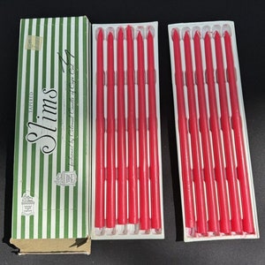 May include: A box of red taper candles labeled "Slims Tapered" and "fashioned by Colonial Candle of Cape Cod". The candles are packaged in two clear plastic trays.