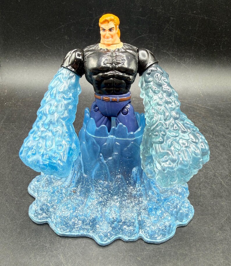 May include: Action figure of a muscular man with orange hair, wearing a black top, blue pants, and a brown belt. The figure has translucent blue water-like arms and is standing in a blue water base. The figure is a collectible toy.
