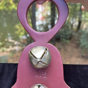 May include: A burgundy leather bell holder with two silver bells and the initials "MPS" embossed on the front.