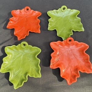 May include: Set of four ceramic maple leaf shaped serving dishes. Two dishes are green and two are orange.