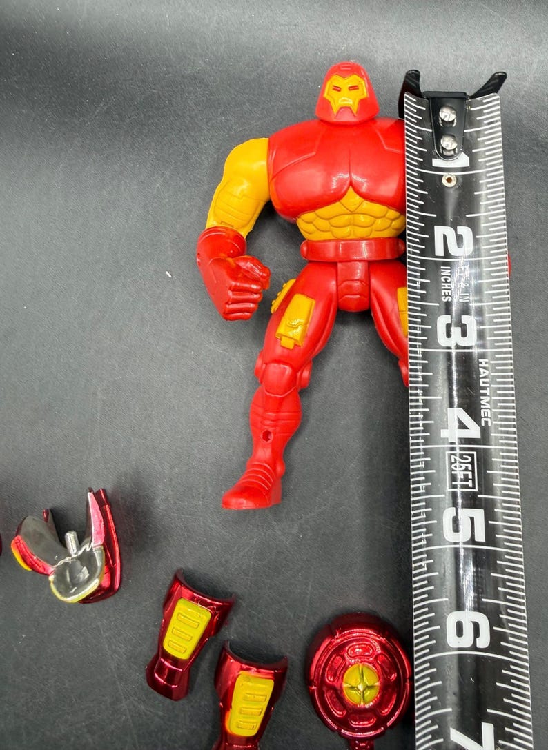 May include: A red and yellow Iron Man action figure, approximately 5 inches tall, with detachable accessories. The figure has a red helmet, chest, and legs, with yellow arms and chest details. Additional red and silver pieces are scattered around.