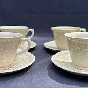 May include: Set of four cream-coloured teacups and saucers with a floral design. The cups and saucers have a raised, embossed pattern.
