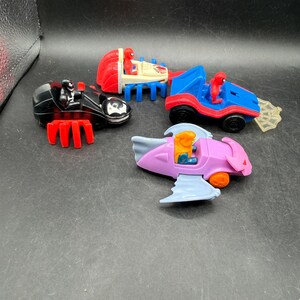 May include: Four toy vehicles featuring Spider-Man characters. Includes a black motorcycle, a red and blue car, a blue and red car with a web, and a pink and blue jet. Each vehicle has a character figure.