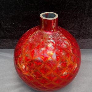 May include: A spherical red glass vase featuring a raised diamond-shaped lattice pattern across its surface. The vase has a short, cylindrical neck with a smooth, circular opening at the top, showcasing a deep, translucent crimson color throughout.