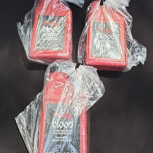 May include: Three red plastic bottles of stage blood, each with a black label that reads "blood" and instructions on how to use the product. The bottles are individually packaged in clear plastic bags.