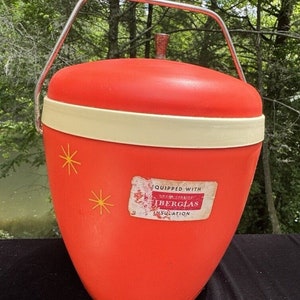 Pode incluir: Um refrigerador vintage vermelho e branco com uma alça de prata. O refrigerador tem um rótulo que diz "Equipped with Owens Corning Fiberglas Insulation".