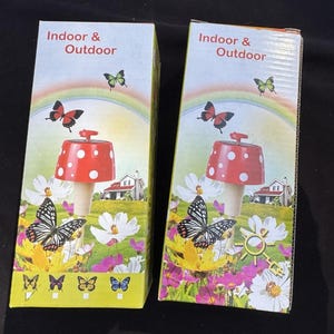 May include: Two boxes featuring images of a red and white mushroom shaped solar powered garden light. The boxes display the text "Indoor & Outdoor". The boxes are adorned with images of butterflies and flowers.