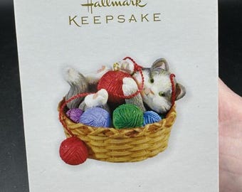 May include: Hallmark Keepsake Christmas ornament featuring a gray and white kitten playing with yarn balls in a wicker basket. The ornament is part of a series and reads "Mischievous Kittens" on the box.