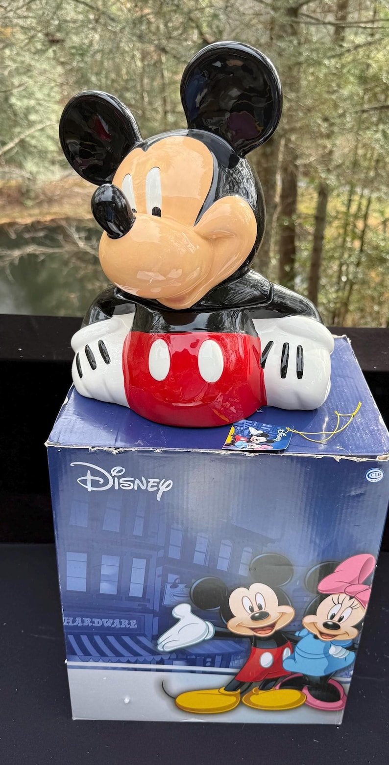 May include: A ceramic Mickey Mouse figure with a black head and ears, a tan face, and a red and white outfit. The figure is on top of a blue Disney box with Mickey and Minnie Mouse graphics.