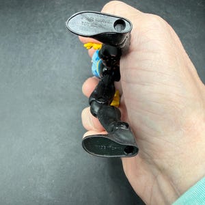 May include: A black and yellow action figure with blue accents. The figure is held in a hand, with the feet of the figure facing the camera. The feet have the text "MADE IN CHINA". The figure is marked "&copy; 1992 MARVEL TOY BIZ".