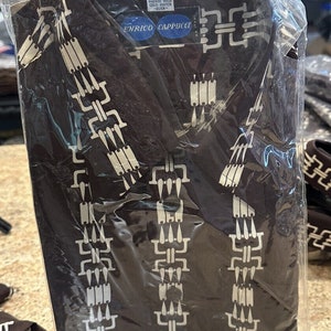 May include: A brown shirt with a white geometric pattern. The shirt is packaged in a clear plastic bag. The label on the shirt reads "100% Polyester Machine Wash Cold Water - Over-" and "Enrico Cappucci".