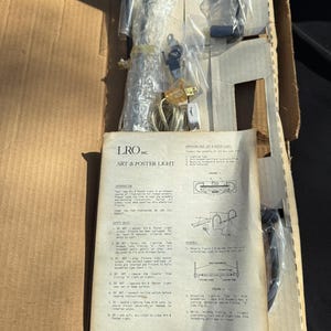 Könnte beinhalten: Nahaufnahme der Anleitung zum Zusammenbauen einer LRO Inc. Art & Poster Leuchte. Die Anleitung enthält Diagramme und Sicherheitshinweise zum Zusammenbauen und Verwenden der Leuchte.