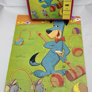 May include: A vintage 70-piece jigsaw puzzle featuring a cartoon blue dog with a red bow tie playing croquet with two gray mice. The puzzle box shows the dog and the text "Every Piece Interlocks".