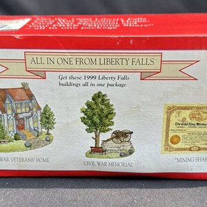 Pode incluir: Uma caixa vermelha com um rótulo branco que diz "Tudo em um de Liberty Falls". O rótulo também diz "Obtenha esses edifícios de Liberty Falls de 1999 todos em um único pacote". A caixa mostra três edifícios em miniatura: uma casa de veteranos da Guerra Civil, um monumento à Guerra Civil e um edifício "Ação de mineração".