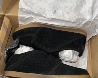Pode incluir: Um par de sapatos de camurça preta com solas marrons. Os sapatos têm um fecho de atacadores e um design perfurado.