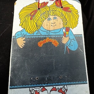 May include: A vintage Cabbage Patch Kids chalkboard with a blue frame and a picture of a Cabbage Patch Kid holding a paintbrush. The chalkboard has a black writing surface and the text "Cabbage Patch Kids" is printed on the bottom.