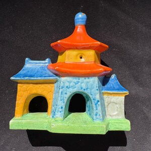 May include: A colorful ceramic pagoda with a multi-tiered design. The pagoda features a vibrant color scheme, including orange, yellow, blue, and green. The structure has arched openings and a detailed roof, showcasing a traditional architectural style.