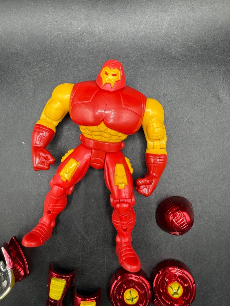 May include: A red and yellow Iron Man action figure with detachable parts. The figure has a red helmet, chest, and legs, with yellow arms and accents. Several red and yellow accessories are scattered around the figure.