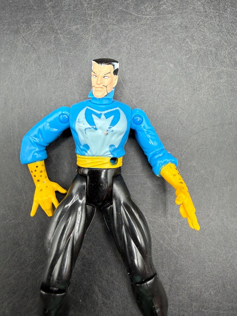 May include: A plastic action figure of a character with a stern expression. The figure wears a blue top with a light blue emblem, black pants, yellow gloves, and a yellow belt. The figure is posed against a gray background.