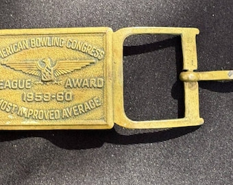 May include: A gold-colored belt buckle with the text "American Bowling Congress League Award 1959-60 Most Improved Average" and a winged eagle design.