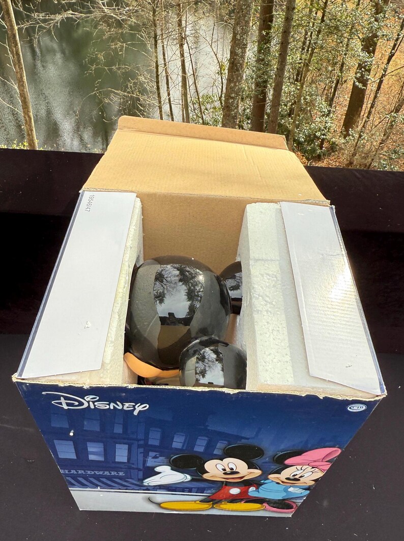 May include: A black Mickey Mouse figurine inside a cardboard box with the Disney logo. The box features illustrations of Mickey and Minnie Mouse. The figurine is glossy and has a round head and ears.