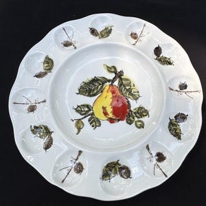 Puede incluir: Plato de servir de cerámica blanca con 12 compartimentos individuales alrededor del borde. El centro del plato presenta un diseño pintado a mano de una pera con hojas verdes.