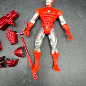 Puede incluir: Una figura de acci&oacute;n de Iron Man roja y plateada con m&uacute;ltiples accesorios. La figura tiene un torso, brazos y piernas rojos, con detalles plateados en los brazos y las piernas. Los accesorios incluyen una pistola roja, un casco y otras piezas.