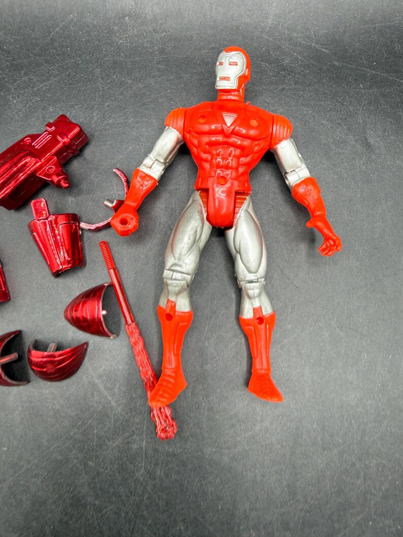 Puede incluir: Una figura de acci&oacute;n de Iron Man roja y plateada con m&uacute;ltiples accesorios. La figura tiene un torso, brazos y piernas rojos, con detalles plateados en los brazos y las piernas. Los accesorios incluyen una pistola roja, un casco y otras piezas.