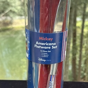 Puede incluir: Un tubo de plástico transparente que contiene un juego de cubiertos Mickey Americana de 12 piezas. El juego incluye 4 tenedores, 4 cucharas y 4 cuchillos. El embalaje presenta un diseño rojo, blanco y azul con las palabras "Mickey Americana Flatware Set" y "Disney store".