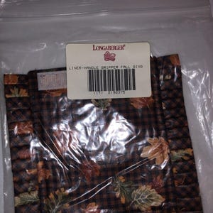 May include: A brown and black fabric pot holder with a fall leaf design and a white label that reads "Longaberger Liner-Handle Gripper Fall Ging (11) 2198375".