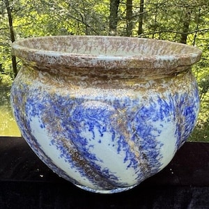 May include: A large, white ceramic planter with a blue and gold glaze. The planter has a rounded, bulbous shape and a wide, flat rim.
