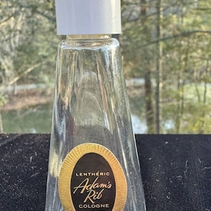 May include: A small, clear glass bottle with a white cap and a gold label that reads "Lentheric Adam's Rib Cologne 1/2 Fl. Oz."