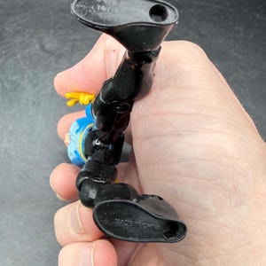 May include: A black and blue action figure with yellow accents. The figure is in a dynamic pose, with one leg extended. The words "MADE IN CHINA" are visible on the foot. The figure is held in a hand.