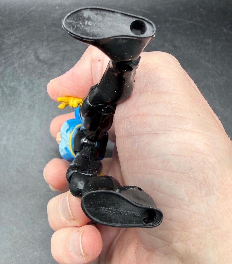 May include: A black and blue action figure with yellow accents. The figure is in a dynamic pose, with one leg extended. The words "MADE IN CHINA" are visible on the foot. The figure is held in a hand.