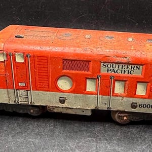 May include: A vintage red and grey Southern Pacific train engine model. The model features the Southern Pacific logo and the number 6000. The train has a weathered appearance, suggesting age and use. A classic toy train.
