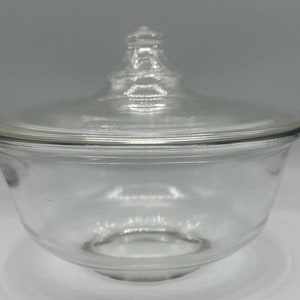 May include: A clear glass bowl with a lid. The bowl is round and has a smooth surface. The lid is also round and has a knob on top.