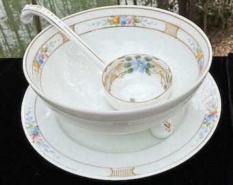 May include: A white porcelain serving bowl with a floral design and gold trim. The bowl is on a matching plate and includes a matching ladle.