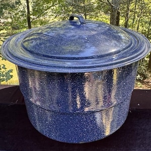 May include: A large, blue speckled enamel pot with a matching lid. The pot has a rounded shape with a wide rim and a black handle on the lid. The speckled pattern is white against the dark blue surface. The pot is designed for cooking.