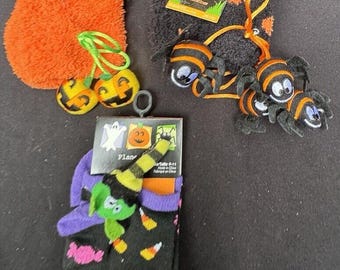Puede incluir: Un conjunto de calcetines con temática de Halloween, que incluye un par de calcetines negros con lunares naranjas, un par de calcetines negros con diseños de maíz dulce y caramelos, y un par de calcetines de felpa naranja. Los calcetines se acompañan de una variedad de accesorios con temática de Halloween, incluidos dos adornos de calabaza naranja, tres arañas negras y naranjas y una abeja negra y naranja.